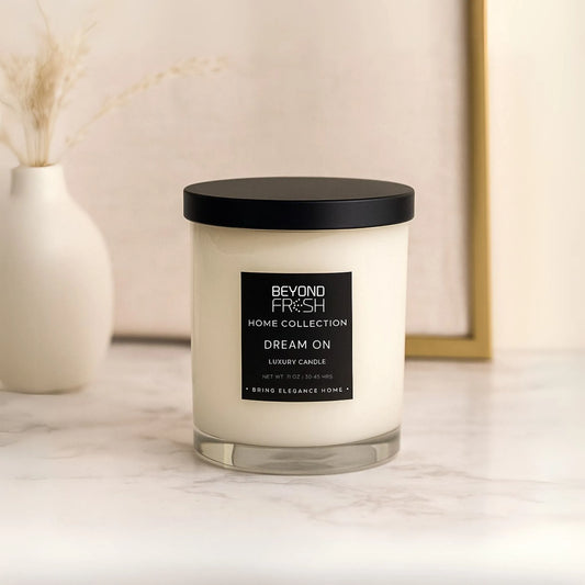 Candle with a black lid and label on a marble surface, Dream On scent with a neutral background.