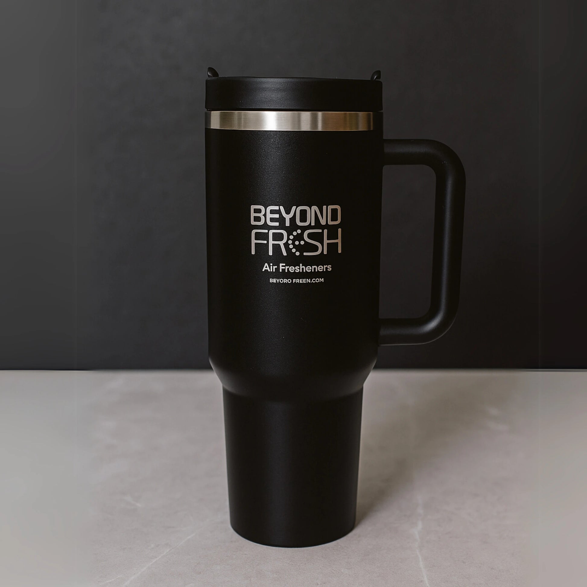Black travel mug with Beyond Fresh branding on a gray surface and dark background